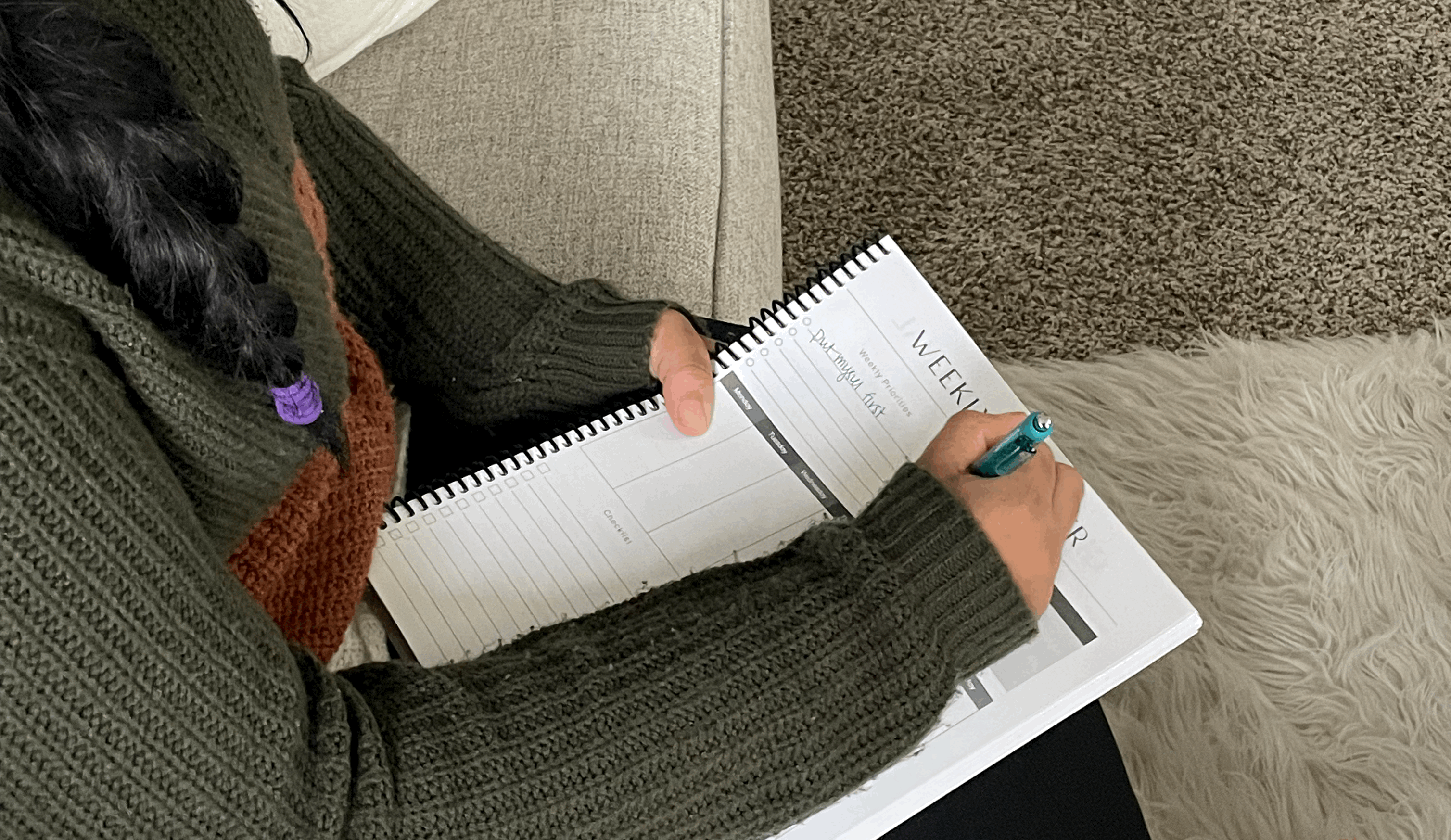 Woman sitting on couch filling out weekly planner page.