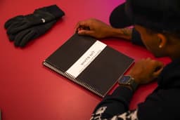Student sitting at desk looking at front cover of Whats Nxt planner in charcoal gray color.