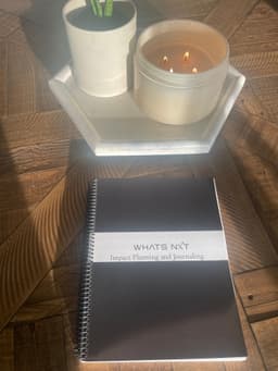 Rose Gold Whats Nxt Planner laying on a table in front of a candle and plant.